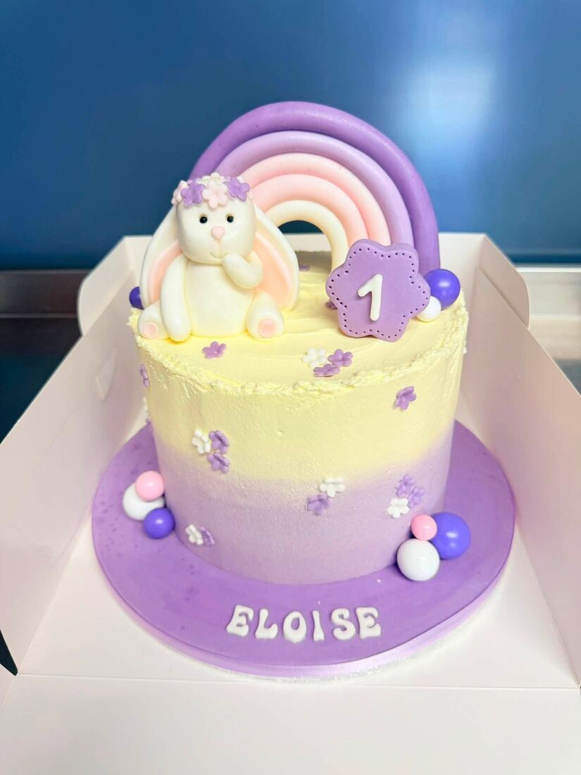 Purple and lemon first-birthday cake with a fondant bunny and rainbow topper