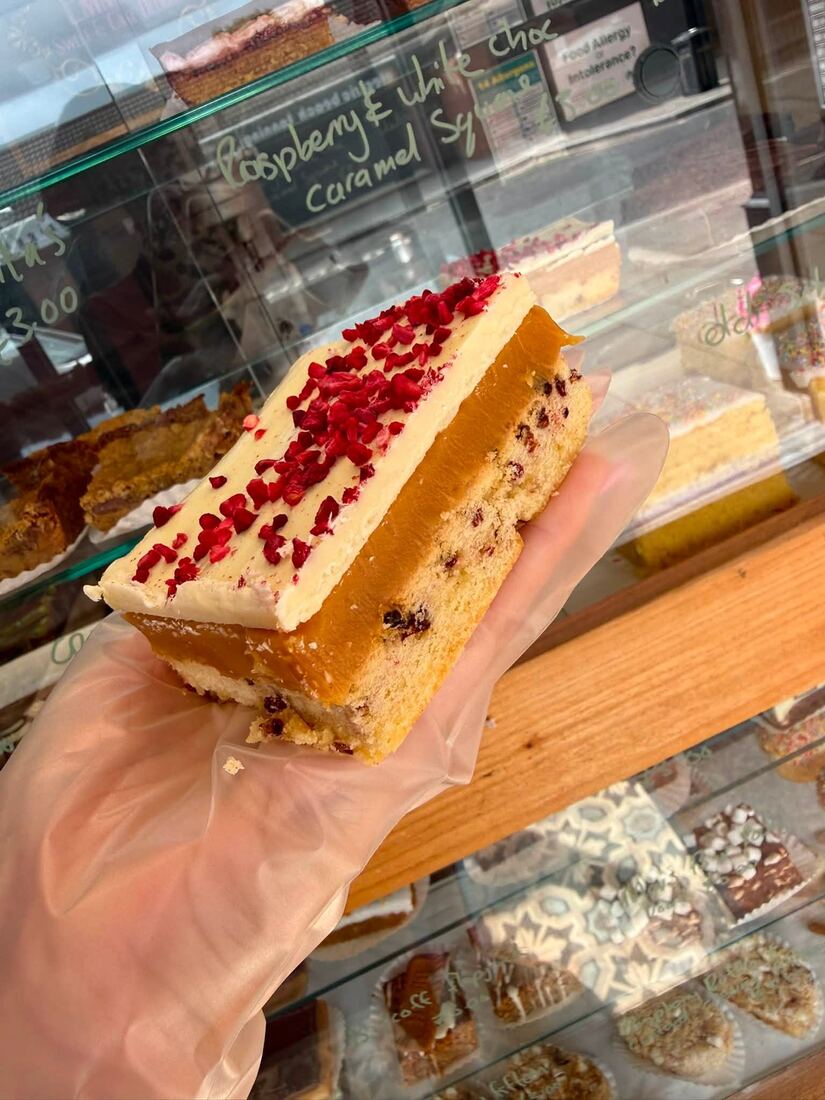 Raspberry and white chocolate caramel square held in front of the bakery counter